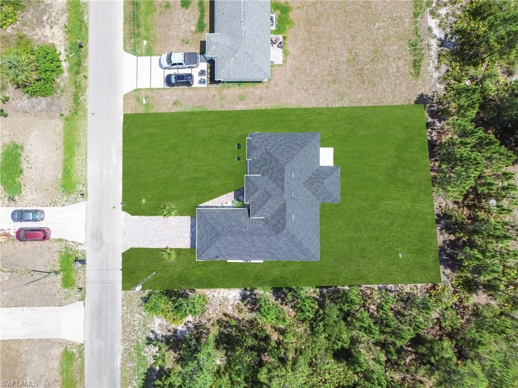 Newly constructed residence featuring a gray shingle roof, expansive green lawn, and a light-toned driveway
