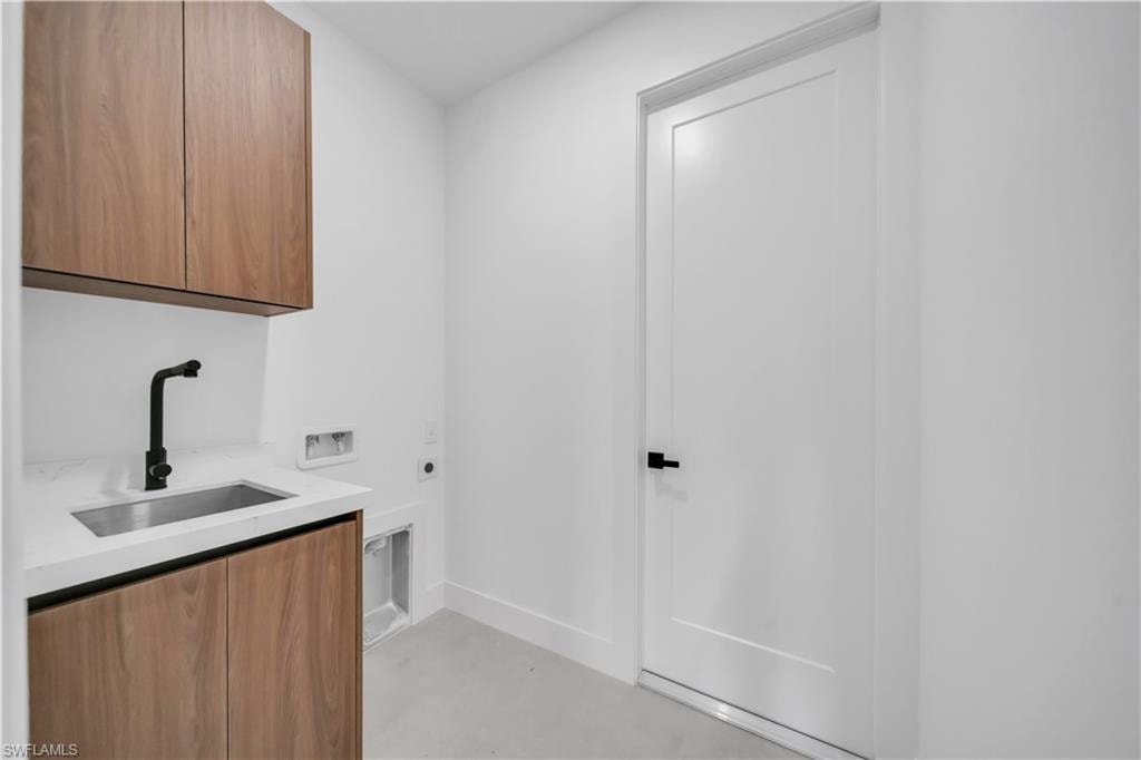 Utility area featuring wood-finish cabinetry, white countertop with an undermount sink, and matte black faucet