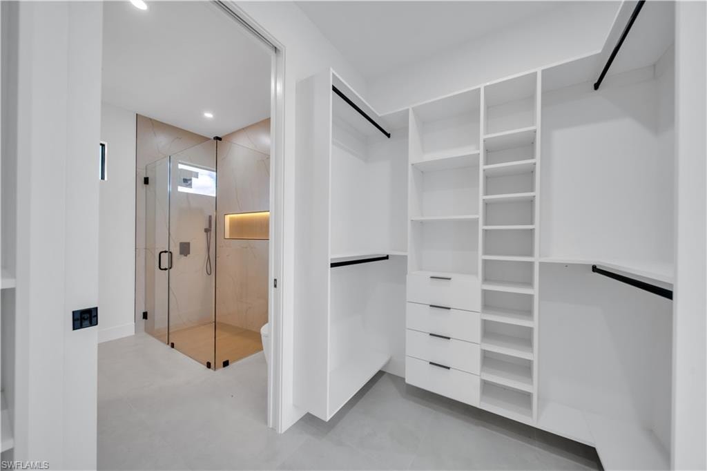 Spacious custom closet with white built-in shelving, multiple drawers with dark hardware, and hanging rods