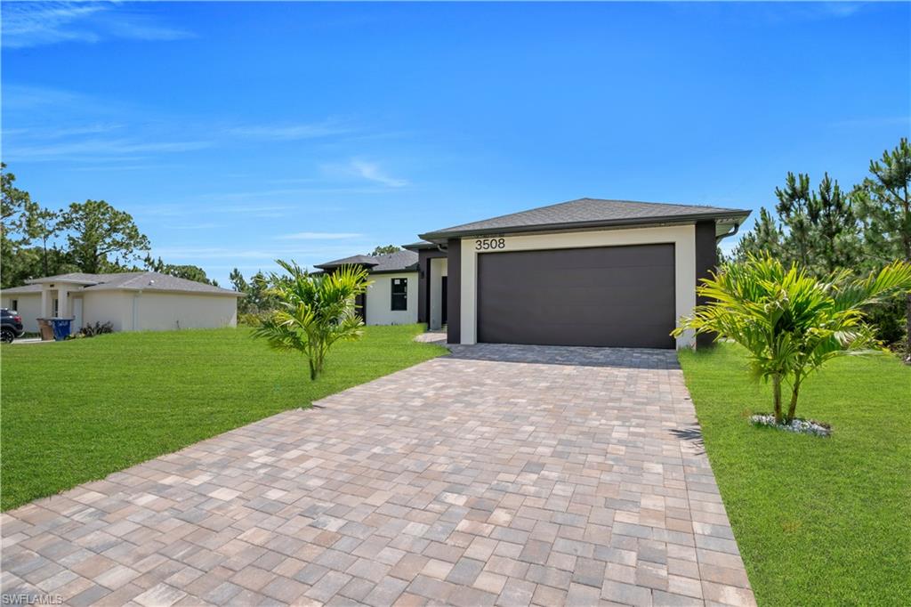 Contemporary exterior featuring a paver driveway, two-car garage, manicured lawn, and tropical landscaping
