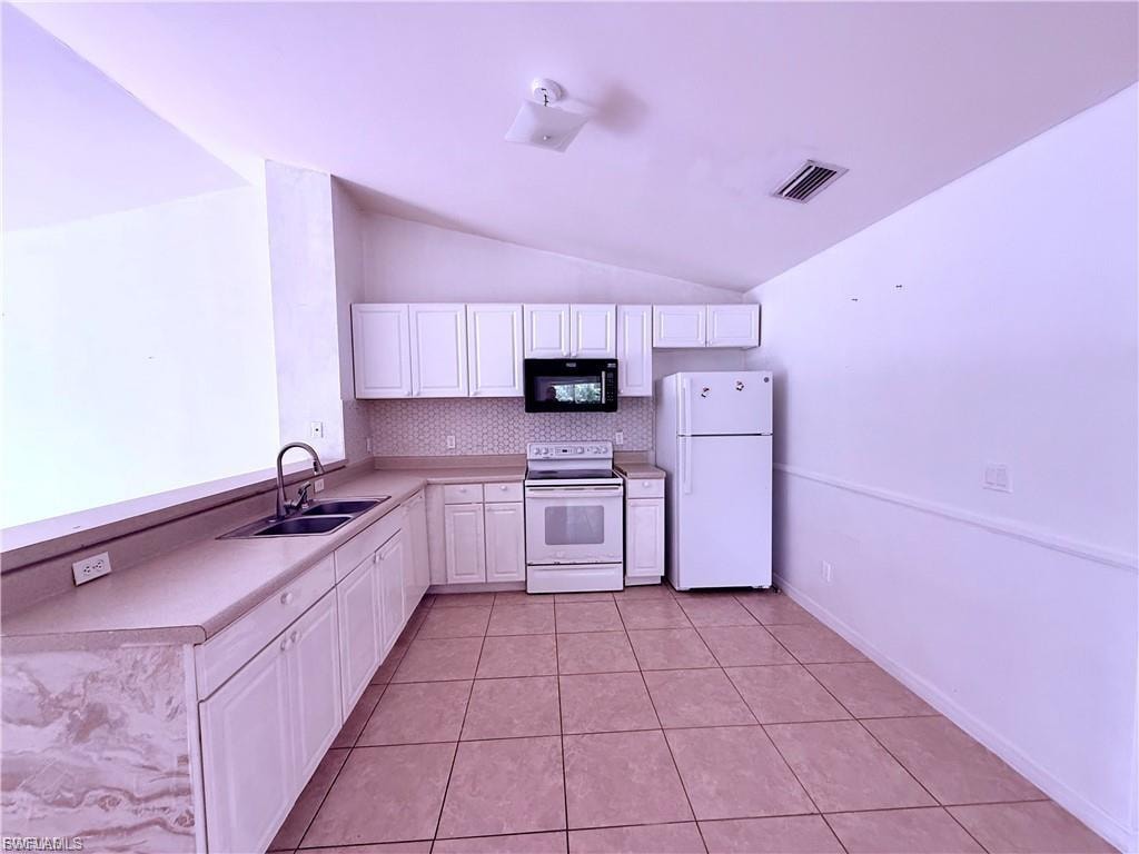 Kitchen with white appliances, vaulted ceiling, light countertops, light tile patterned floors, and tasteful backsplash