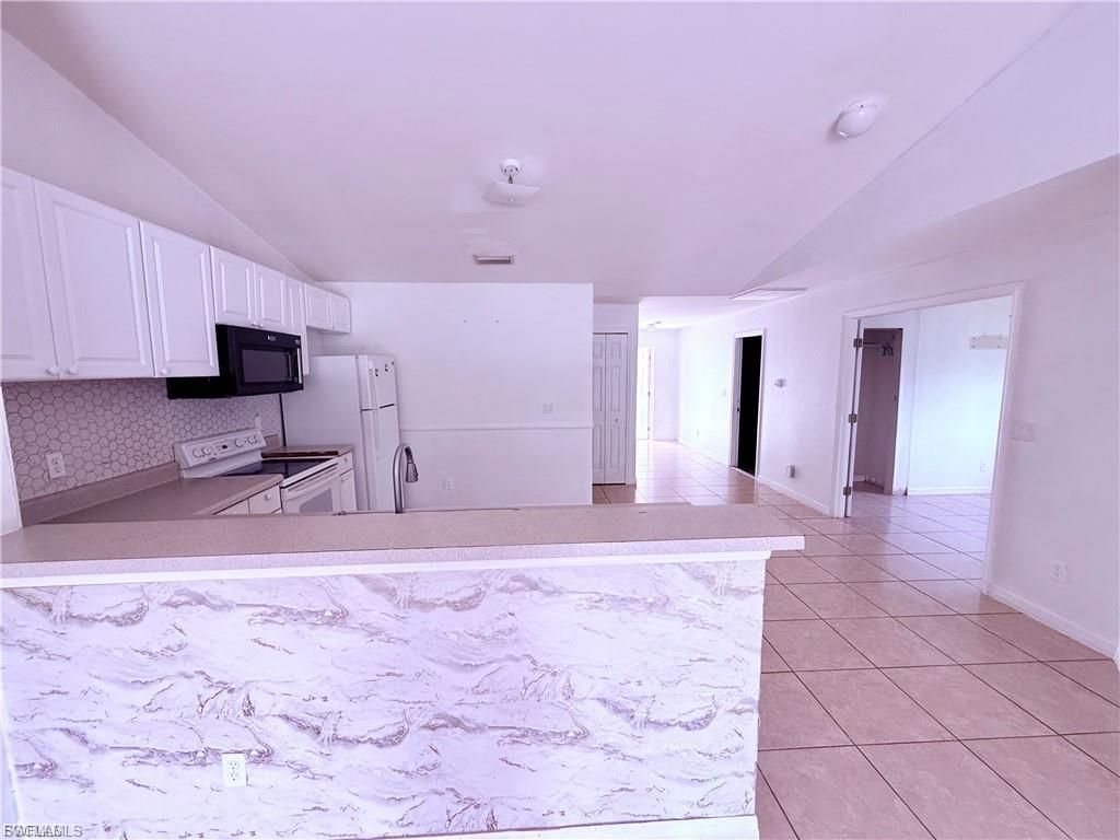 Kitchen with lofted ceiling, light countertops, white range with electric cooktop, light tile patterned flooring, and white cabinetry