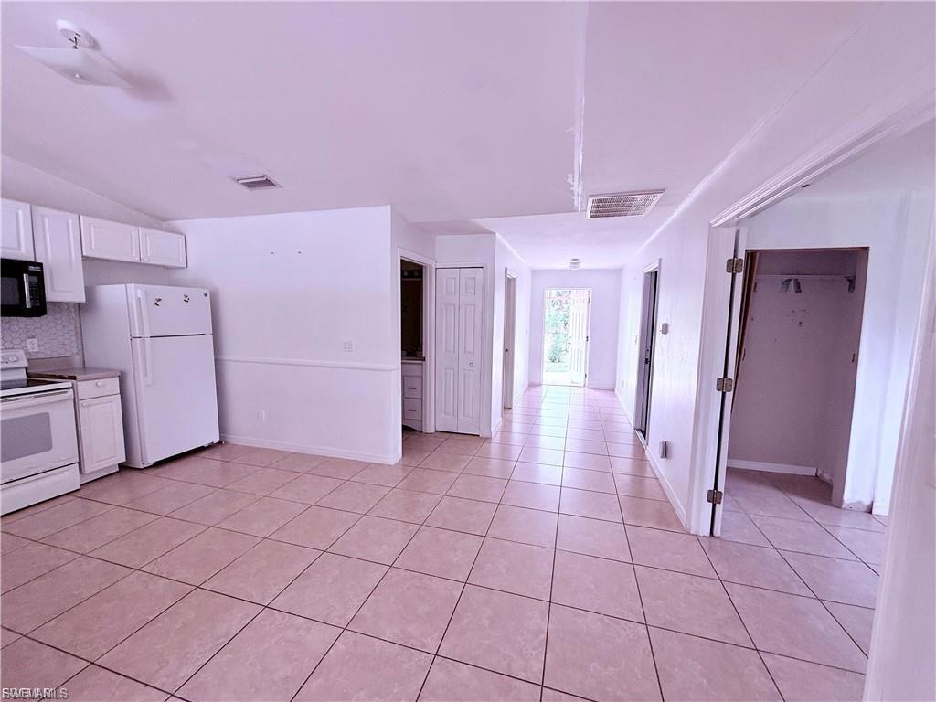 Kitchen featuring white appliances, white cabinetry, light countertops, light tile patterned floors, and vaulted ceiling