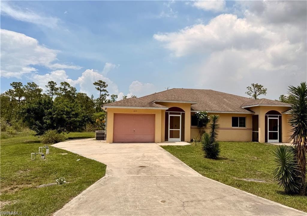 Ranch-style home featuring stucco siding, a front yard, concrete driveway, a garage, and roof with shingles