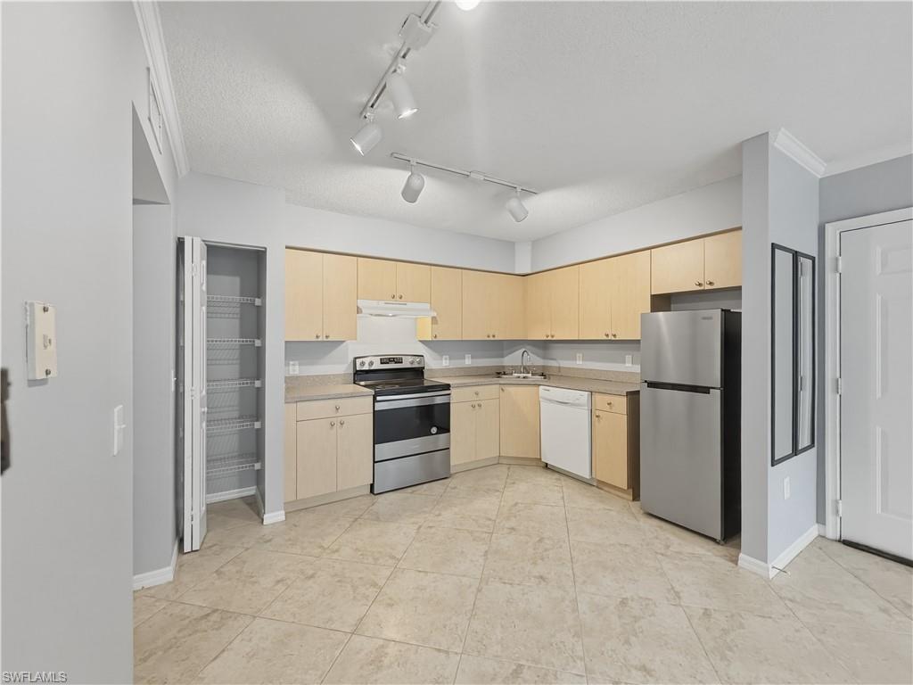 Kitchen featuring light wood-finish cabinetry, stainless steel appliances, a white dishwasher, and track lighting