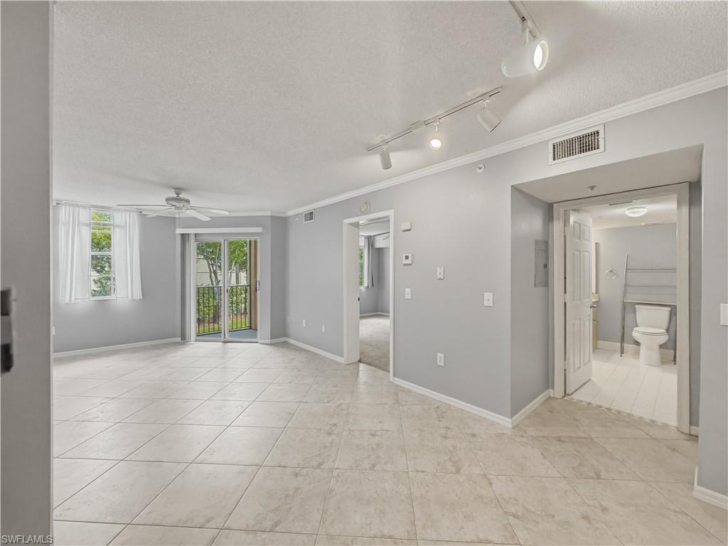 Spacious living area featuring tile flooring, ceiling fan, track lighting, and sliding glass doors opening to an exterior balcony
