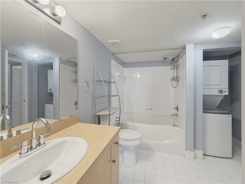 Bathroom featuring a full vanity with an integrated sink, a full bathtub with a shower, a stacked washer and dryer, and white tiled flooring