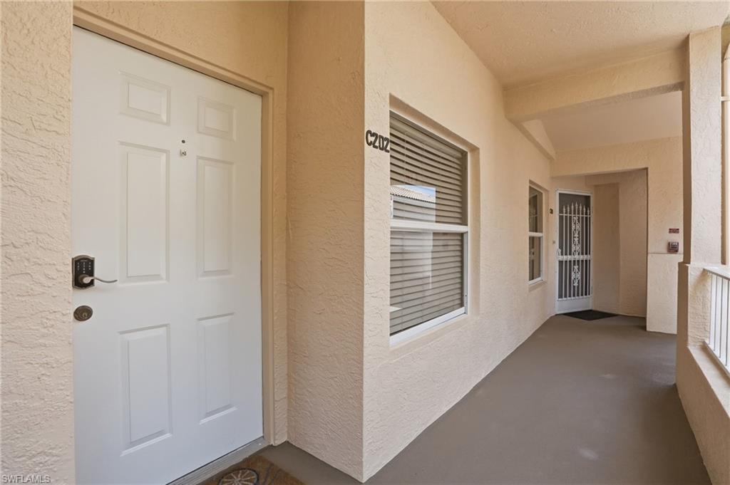 Entryway featuring a white paneled door with a keyless lock, textured exterior walls, an overhead light fixture, and a window with horizontal blinds