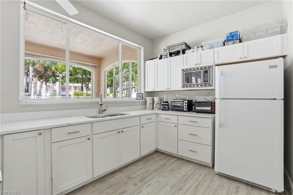 Kitchen with extensive white cabinetry, light-toned wood-finish flooring, and a large window above the sink