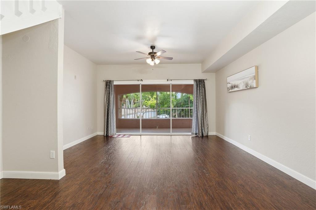 Spacious interior featuring wood-finish flooring, light-toned walls, a ceiling fan with integrated lighting, and a large sliding glass door opening to an outdoor patio with railings