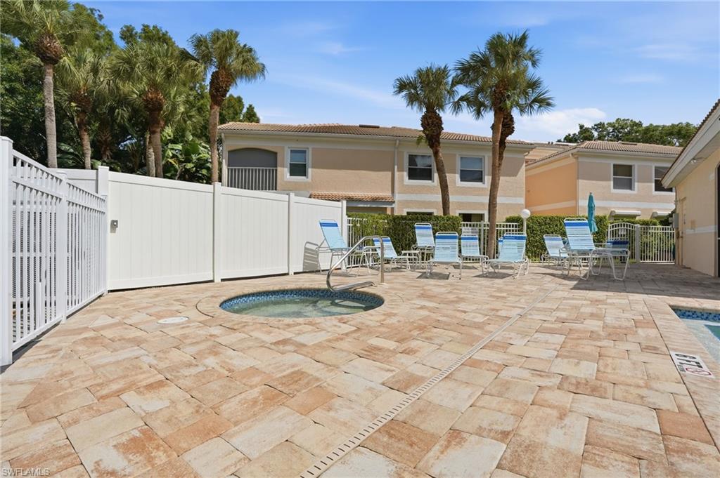 Outdoor spa and pool deck featuring stone pavers, a white privacy fence, and multiple palm trees