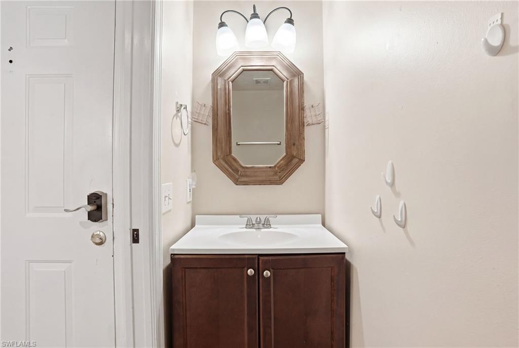 Bathroom vanity featuring a rectangular wood-framed mirror, white countertop, dark wood-finish cabinetry, and a three-light fixture