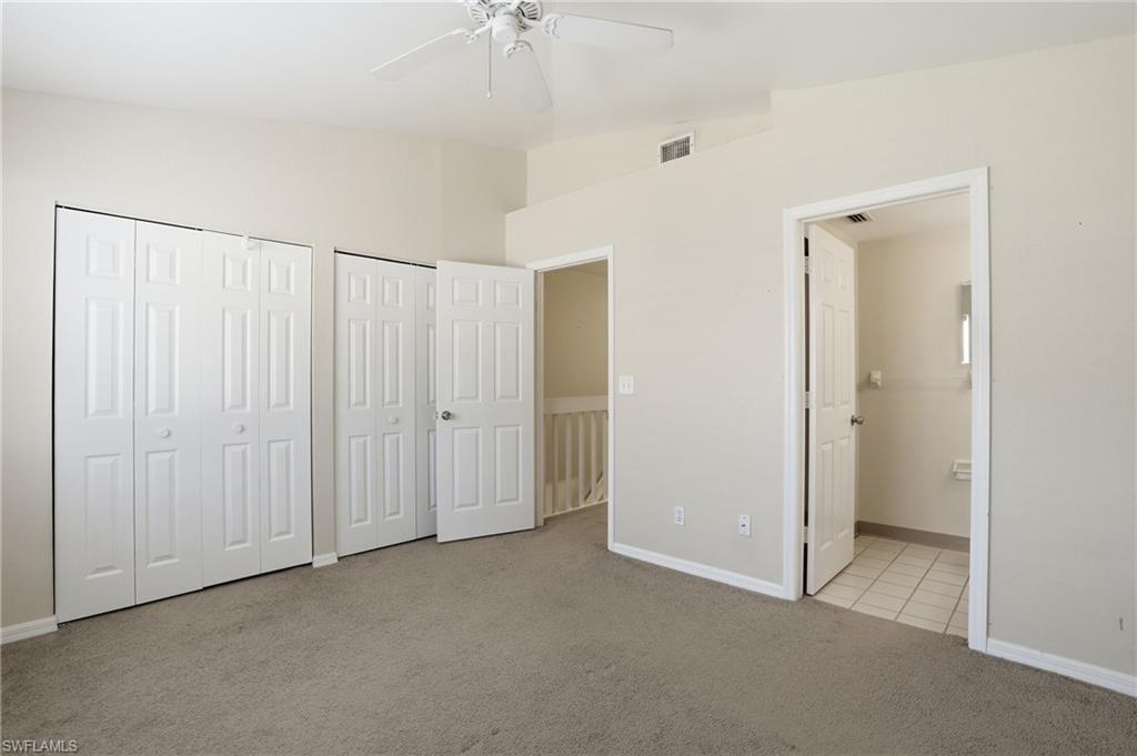 Carpeted room featuring a ceiling fan, two bifold closet doors, a paneled door to another room, and a second paneled door opening to a tiled area