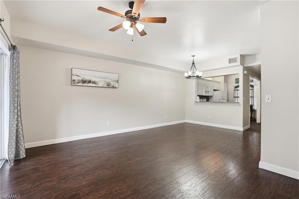 Spacious living area featuring rich wood-finish flooring, a ceiling fan, and a contemporary chandelier