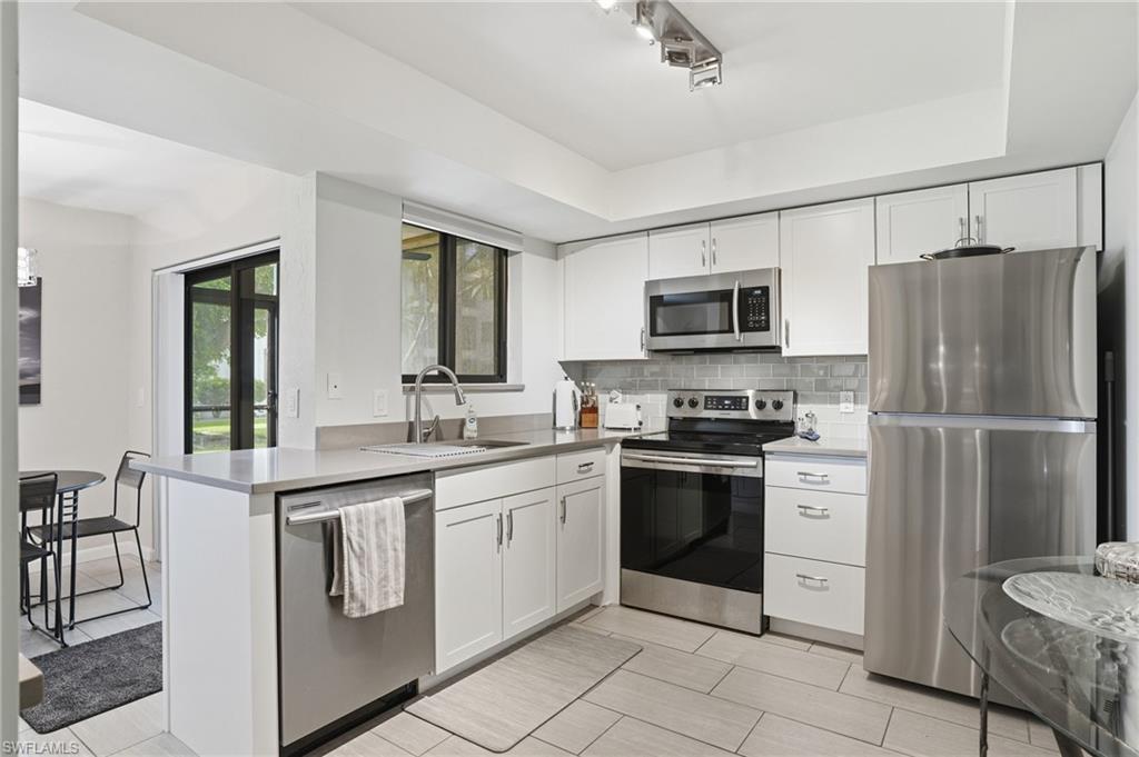 Modern kitchen featuring stainless steel appliances, white cabinetry, light gray countertops, a subway tile backsplash, and light-toned tile flooring