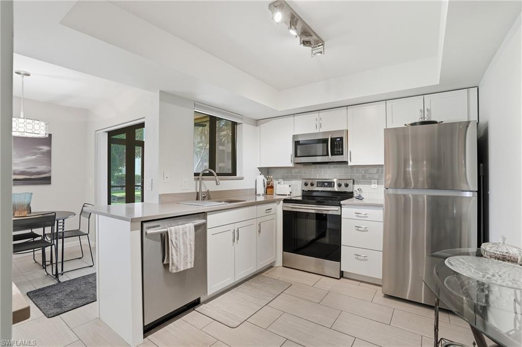 Modern kitchen featuring stainless steel appliances, white cabinetry, a light-toned countertop, a tile backsplash, and neutral tile flooring