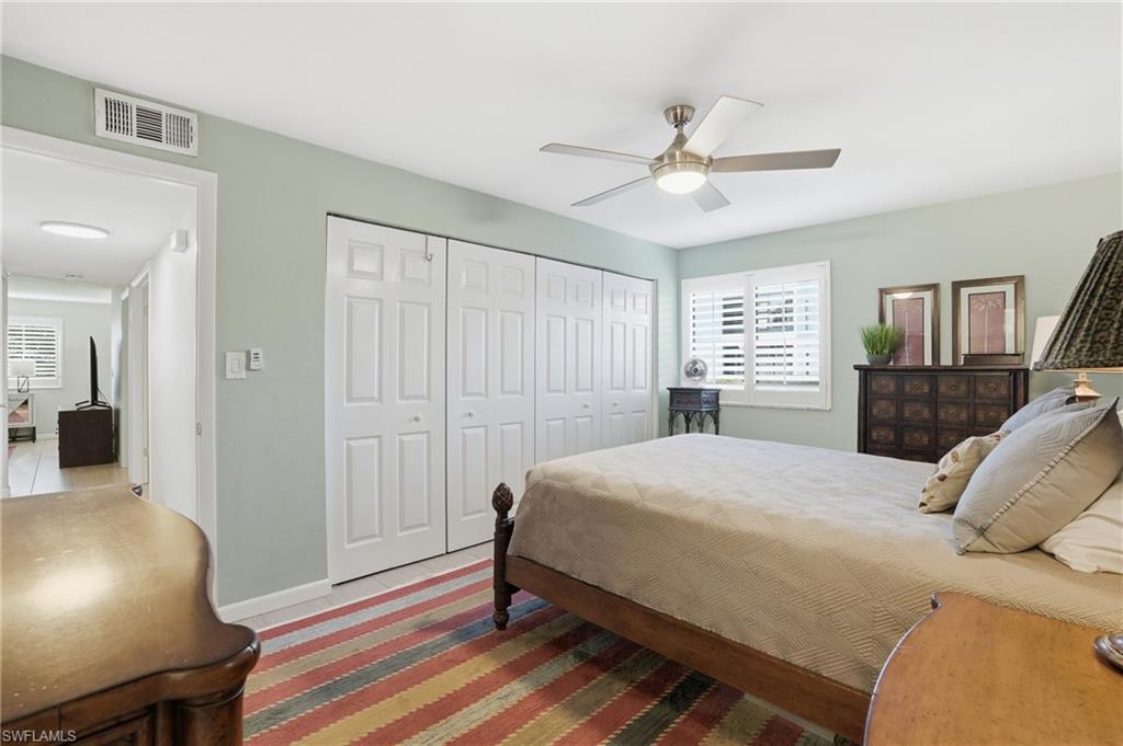 Bedroom featuring a ceiling fan with integrated lighting, window with white plantation shutters, and extensive bi-fold closet doors