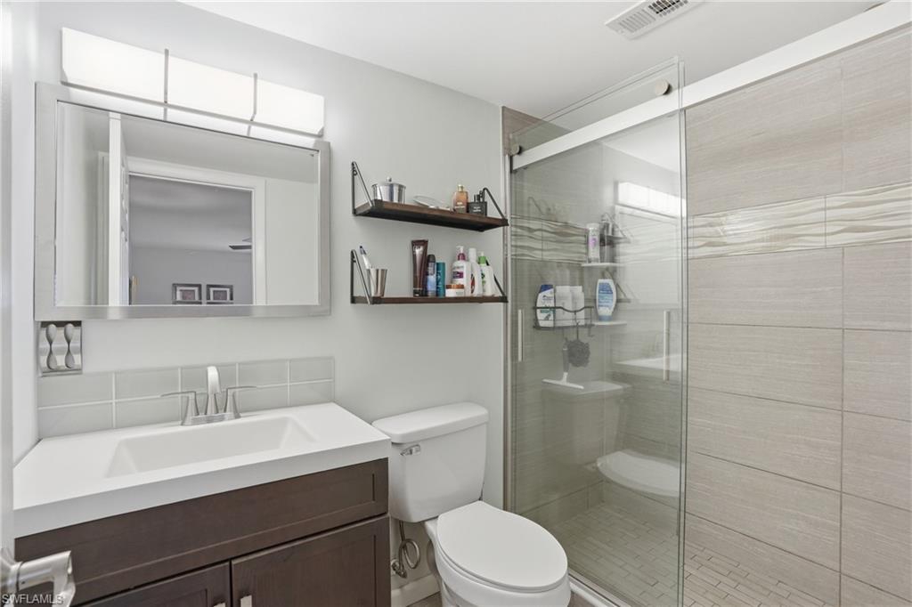 Contemporary bathroom featuring a dark wood-finish vanity with an integrated sink, a rectangular mirror, a sliding glass shower enclosure, a tiled shower interior with textured accent banding, and a white toilet