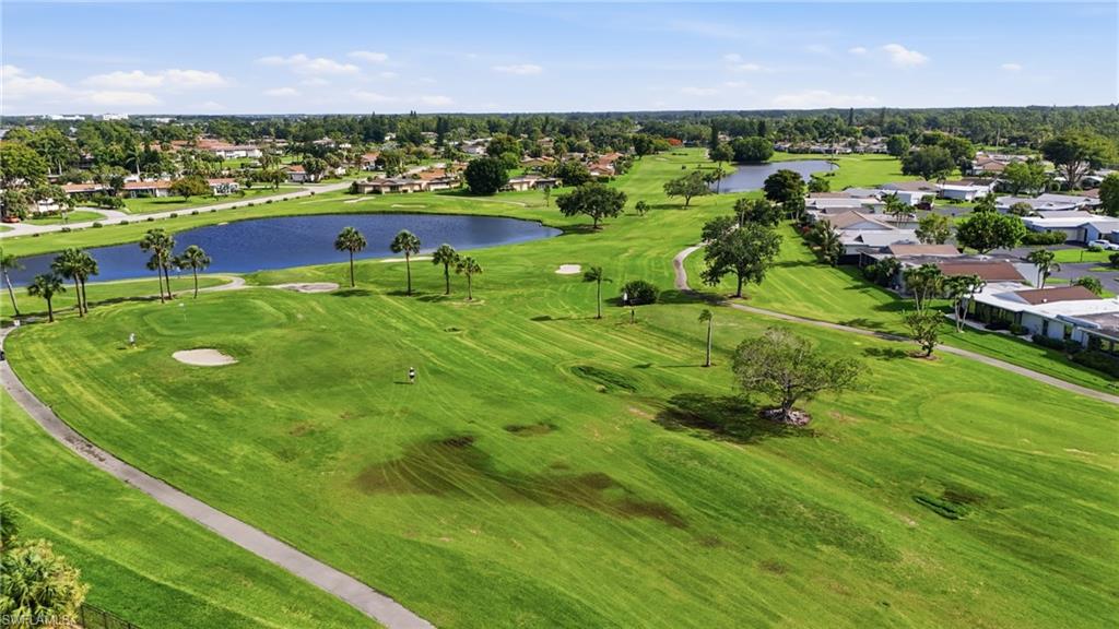 Expansive green golf course featuring mature trees, paved cart paths, and a large water feature