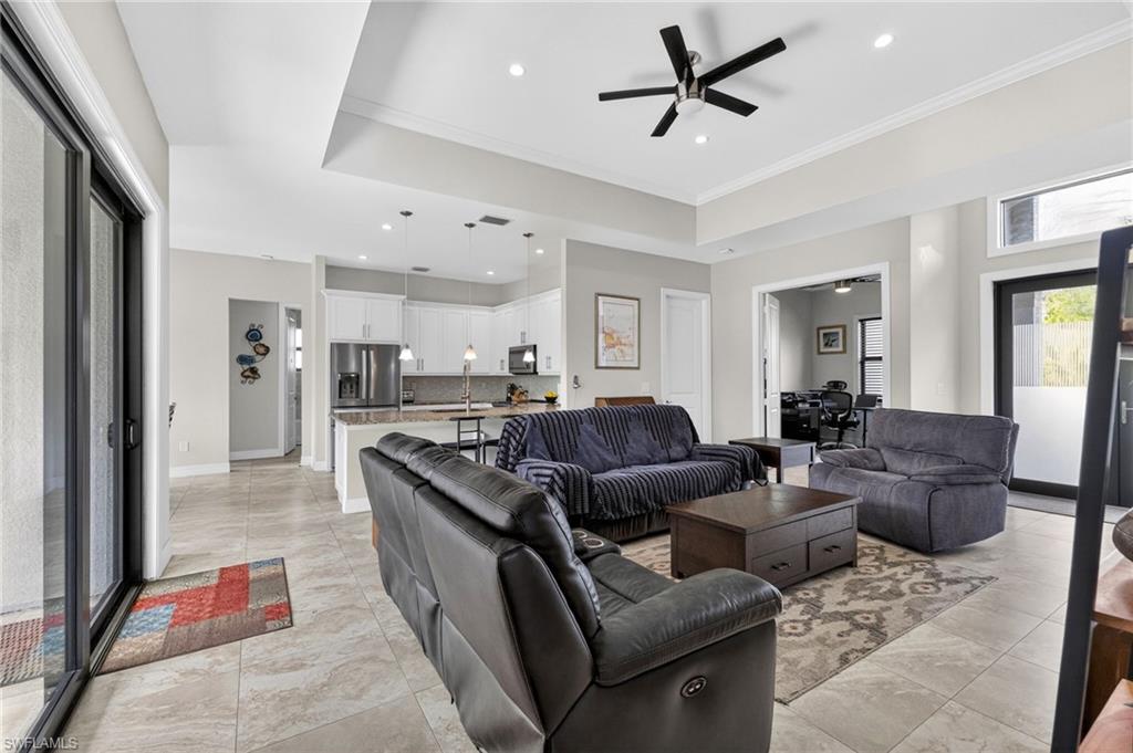 Expansive open-concept living area featuring tile flooring, a tray ceiling with a contemporary ceiling fan, and recessed lighting