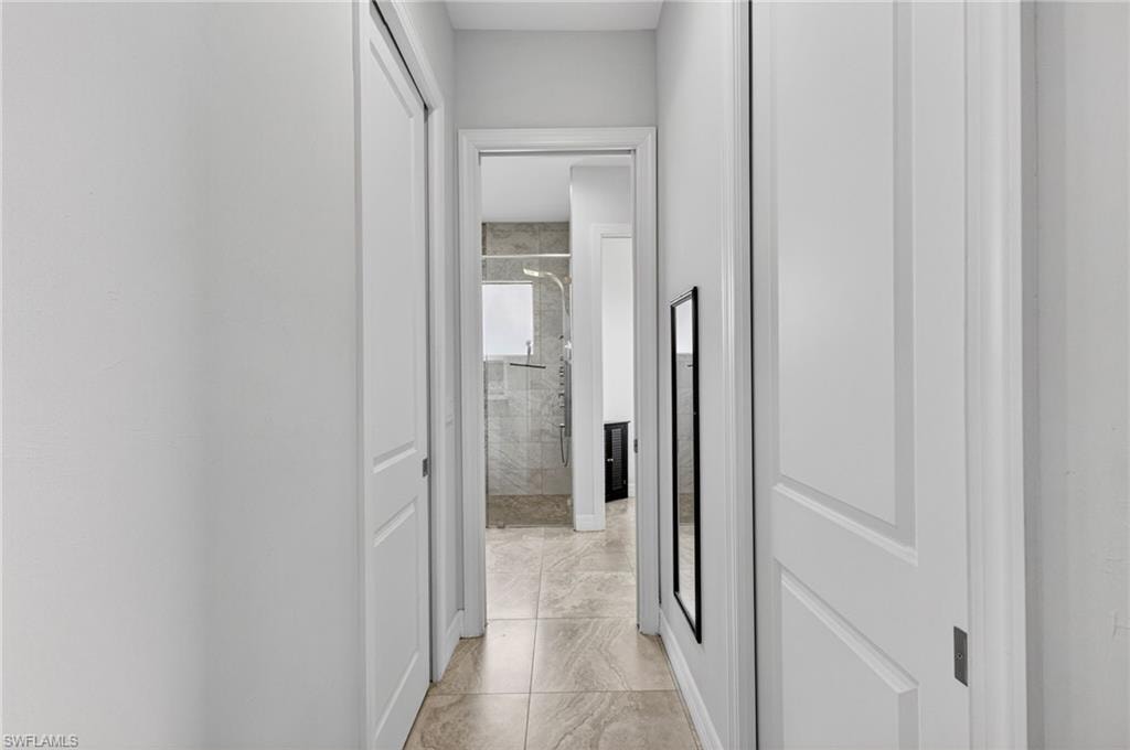 Neutral-toned tile flooring extends through this hallway, featuring crisp white walls and paneled doors