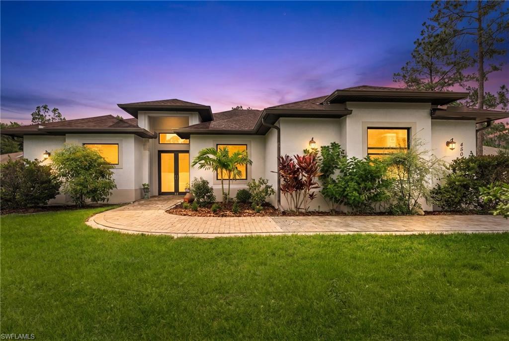 Contemporary stucco exterior featuring a prominent double-door entry with transom window, a curved paver walkway, and integrated landscaping