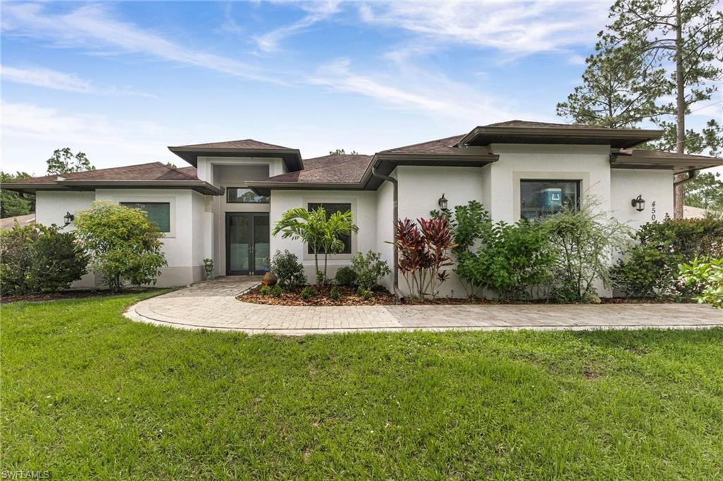 Contemporary white stucco exterior with a prominent entryway, a stone paver circular driveway, and mature landscaping