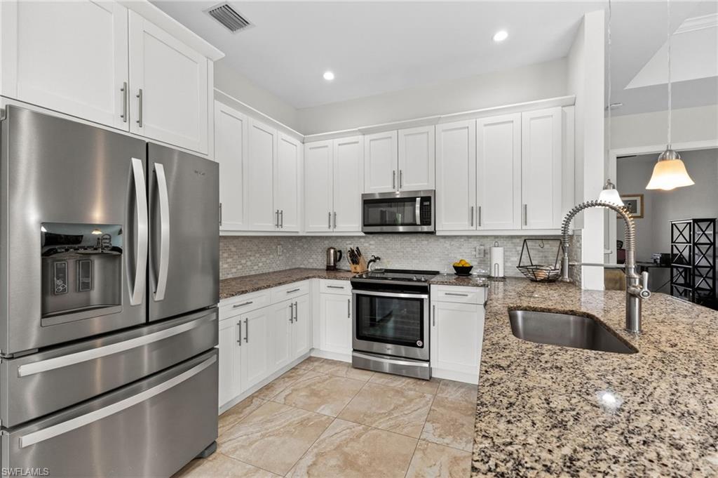 Kitchen featuring white cabinetry, stainless steel appliances, speckled stone countertops, and a tile backsplash