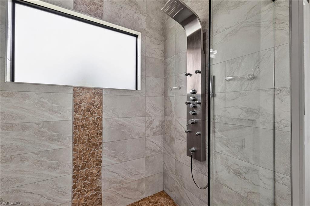 Shower with a multi-function brushed metal shower panel, glass enclosure, and stone-look rectangular wall tiles