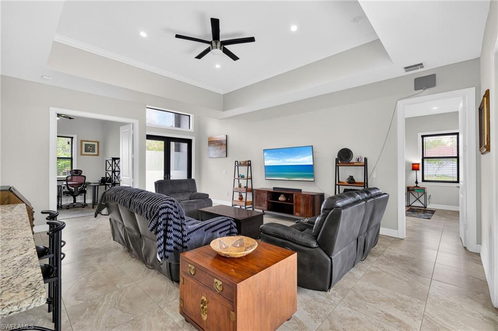 Spacious living area featuring neutral-toned tile flooring, tray ceilings with recessed lighting, and a ceiling fan