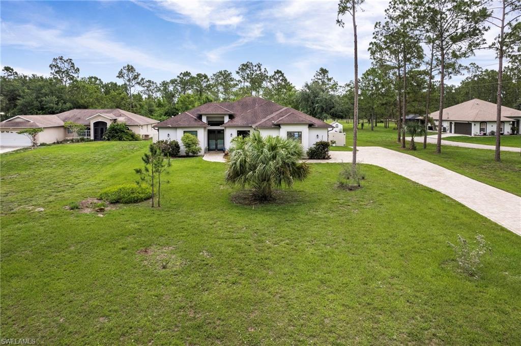 White stucco residence featuring a dark tile roof, a curved driveway, and mature landscaping