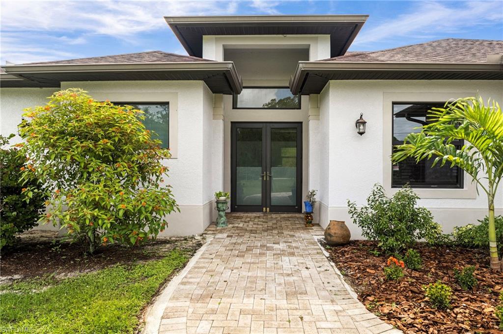 Contemporary stucco exterior with a tiled roof, featuring a paver walkway and mature landscaping