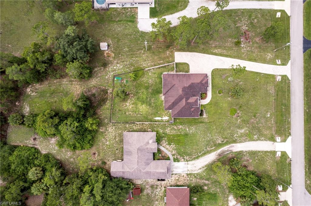 Aerial view showcasing a residential property with a brown-shingled roof and a curved concrete driveway