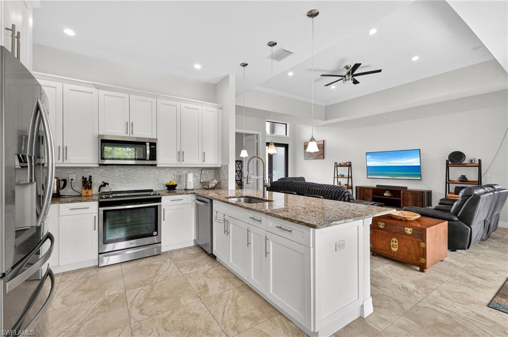 Kitchen featuring white shaker cabinetry, stainless steel appliances, a mosaic tile backsplash, and a large central island with a granite countertop