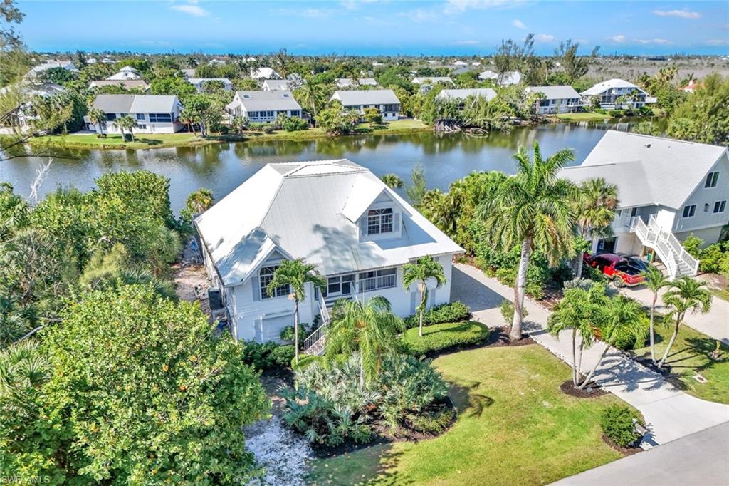 Waterfront property featuring a metal roof, mature tropical landscaping, a private driveway, and a waterside patio area