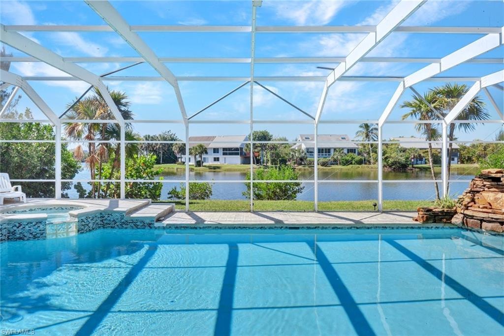 Screened pool enclosure featuring a large pool, integrated spa, and a natural stone-look waterfall structure