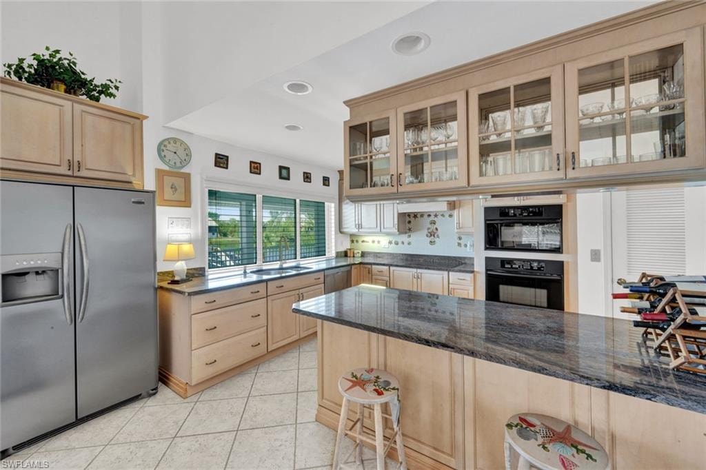 Kitchen featuring light wood cabinetry, a built-in double oven, a stainless steel side-by-side refrigerator, and a kitchen island with a dark countertop