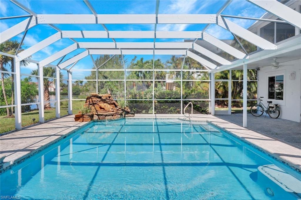 Screen-enclosed swimming pool featuring a rock waterfall, concrete deck, and pool steps