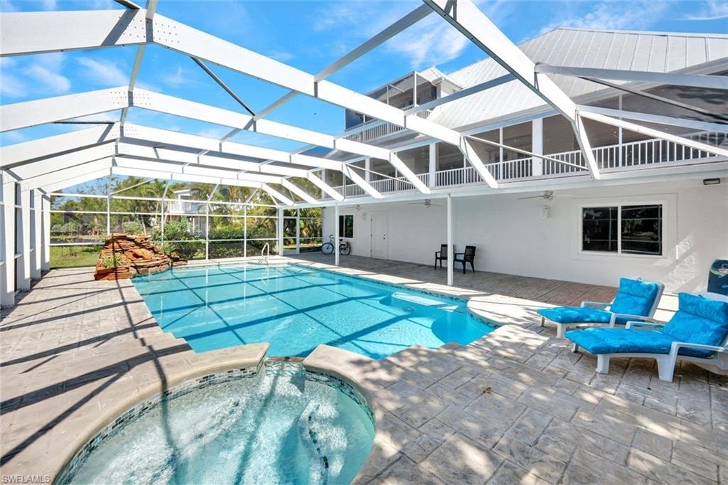 Screened-in pool area featuring a rectangular swimming pool, integrated hot tub with mosaic tile accents, and a rock waterfall feature