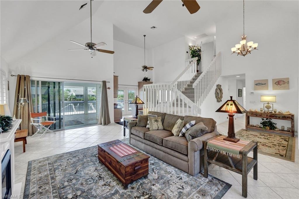 Vaulted ceilings accentuating a spacious interior with large sliding glass doors, tile flooring, a staircase with white railings, and a built-in fireplace