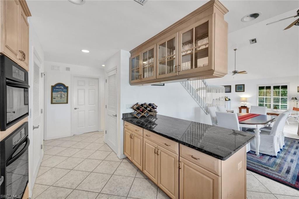 Kitchen counter with granite-finish countertop, light wood-finish cabinetry, and upper glass-front display cabinets