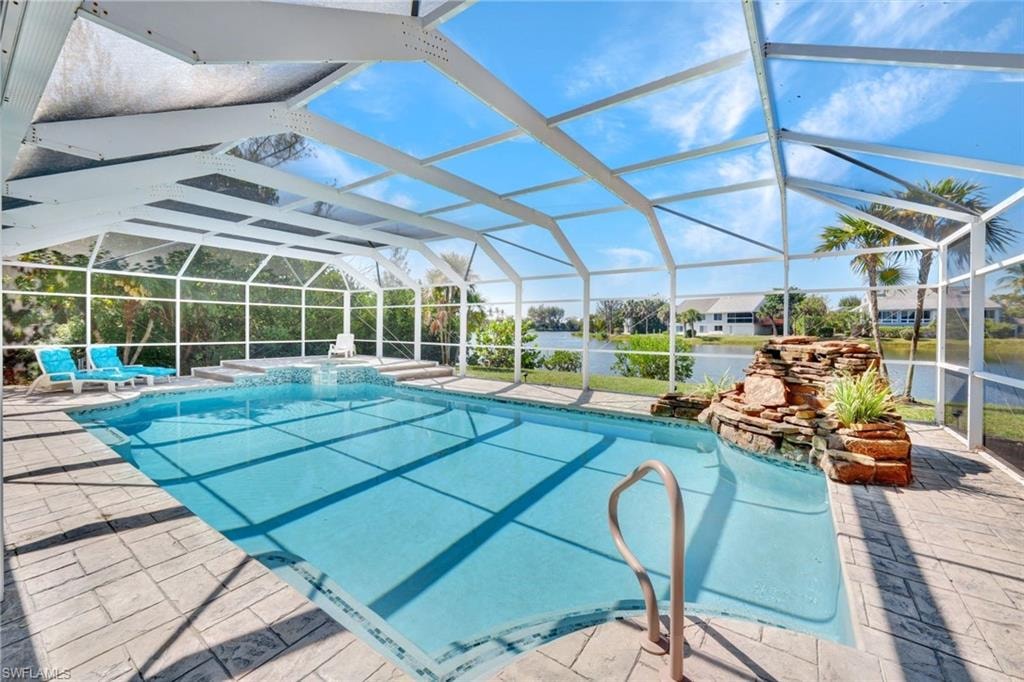 Screen-enclosed pool area featuring a built-in spa, rock waterfall feature, and ample deck space with stamped concrete pavers