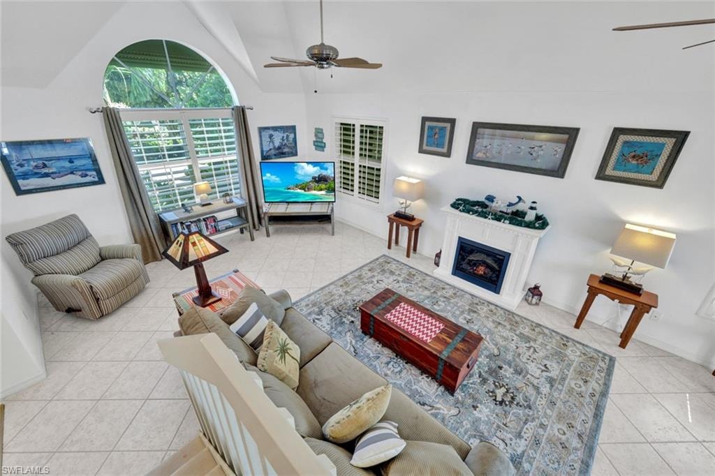 Vaulted ceiling living area featuring a large arched window, ceiling fan, and tile flooring