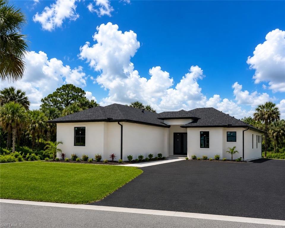 Contemporary stucco exterior with a dark asphalt shingle roof, black-framed windows, a deep black paved driveway, and manicured landscaping featuring palm trees and shrubs