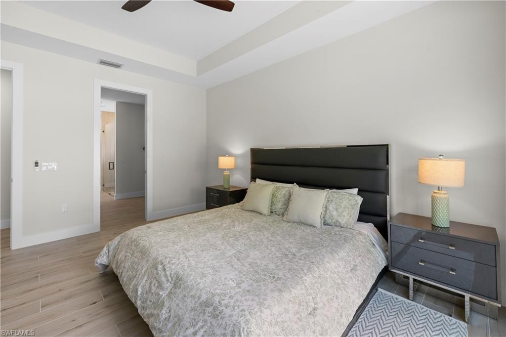 Bedroom featuring wood-finish tile flooring, tray ceiling, and a ceiling fan