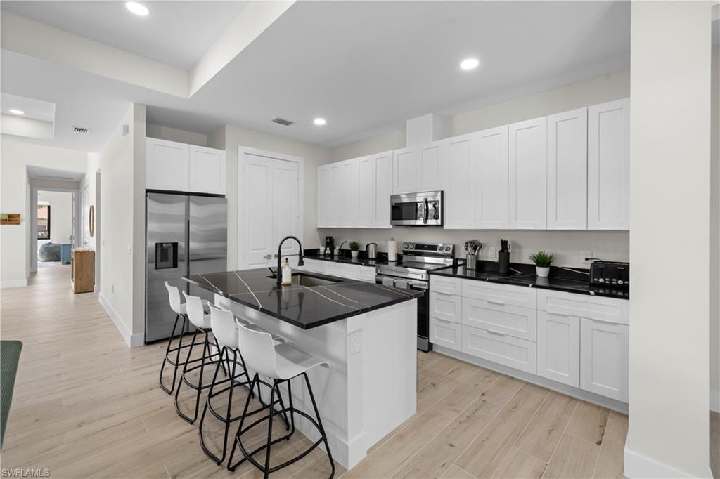 Modern kitchen featuring an expansive island with a dark countertop, white shaker cabinetry, stainless steel appliances, and wood-finish flooring
