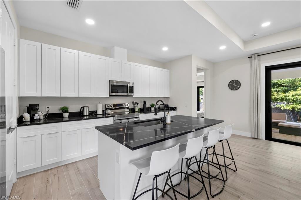 Modern kitchen featuring a black stone-finish island with seating, extensive white cabinetry, stainless steel appliances, and wood-finish flooring
