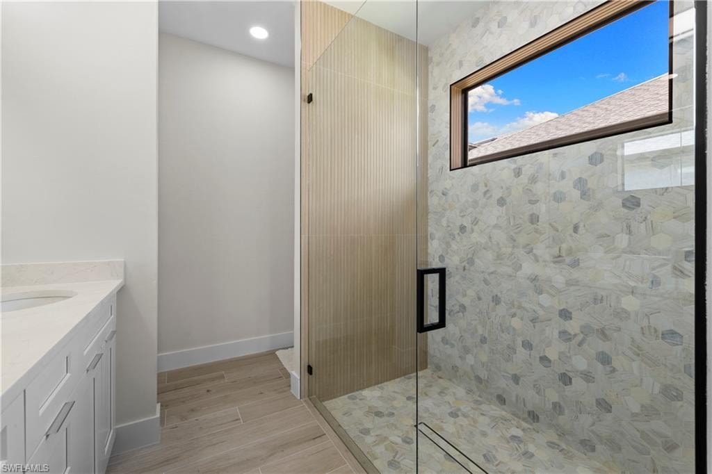 Contemporary bathroom featuring a frameless glass shower enclosure, a white shaker vanity with a light-toned countertop, and wood-finish flooring
