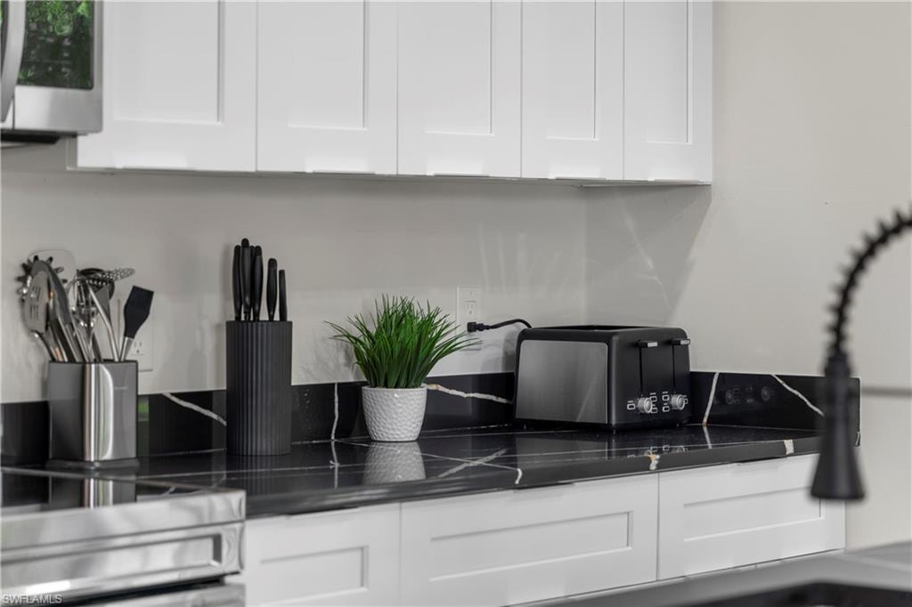 Kitchen featuring white shaker-style cabinetry, black countertops with white veining, and a black backsplash