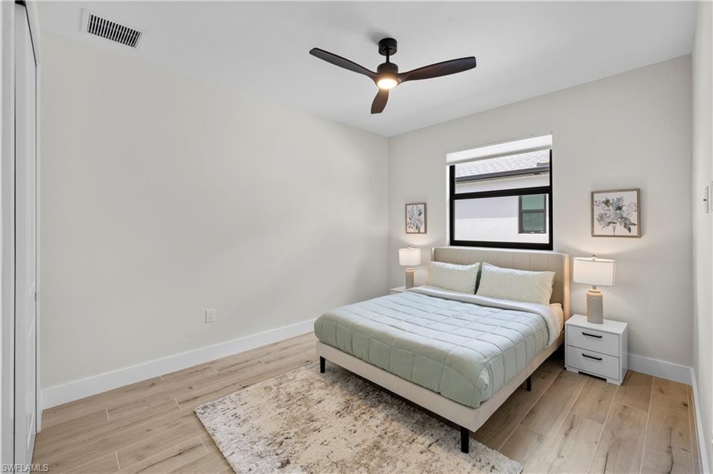 Bright room featuring wood-finish flooring, a modern black ceiling fan with integrated lighting, a large window with black framing, and white baseboards
